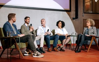 Trois hommes et deux femmes assis, un micro à la main, intervenant lors d'un colloque.